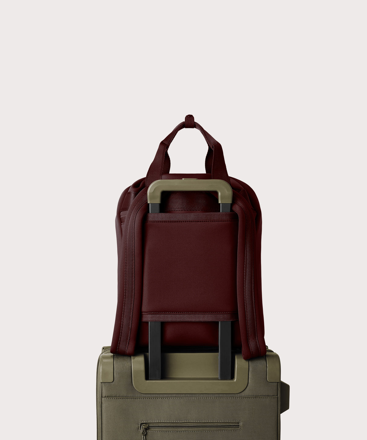 Rhys Backpack in a deep brown with purple undertones strapped to luggage with the neoprene luggage-handle sleeve.