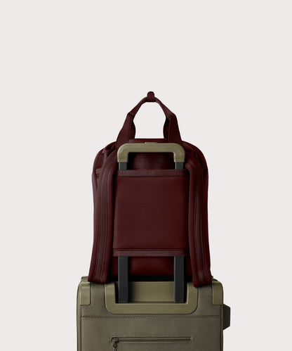 Rhys Backpack in a deep brown with purple undertones strapped to luggage with the neoprene luggage-handle sleeve.